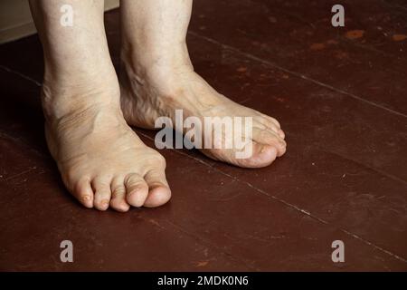 pieds d'une vieille grand-mère sur un plancher en bois sale, solitude, pieds d'un vieil homme, pensionné dans la pauvreté Banque D'Images