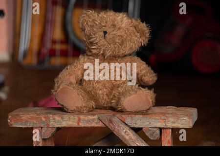 vieux ours en peluche sale est assis sur un banc dans une pièce sombre à la maison, abandonné et solitaire, la pauvreté Banque D'Images