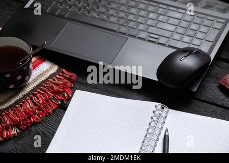 un bloc-notes noir pour ordinateur portable avec de l'argent pour le café se trouve sur la table de travail en bois noir, un ordinateur portable sur la table de travail pendant le travail, processus créatif, indépendant Banque D'Images