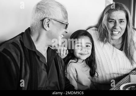 Heureux grands-parents latins ayant plaisir à manger avec la petite-fille à la maison de patio - Focus sur le visage de fille - montage noir et blanc Banque D'Images