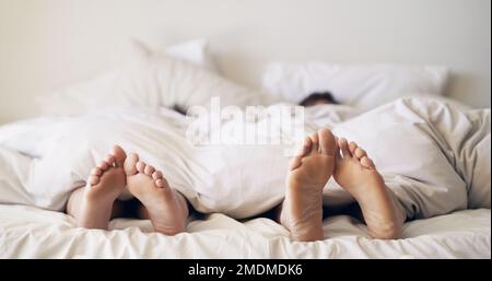 Entwiné dans un havre d'amour. un couple pieds poking dehors de sous les draps de lit. Banque D'Images