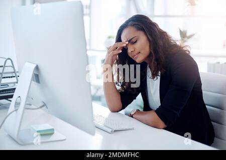 Ma tête a l'impression d'exploser. une jeune femme d'affaires qui regarde stressée en travaillant sur un ordinateur dans un bureau. Banque D'Images