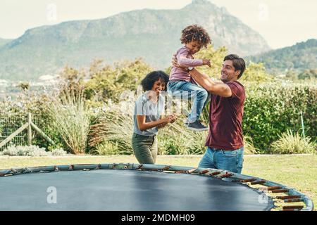 Il apporte un monde de plaisir dans nos vies. un adorable petit garçon sautant sur un trampoline avec ses parents regardant en arrière-plan. Banque D'Images