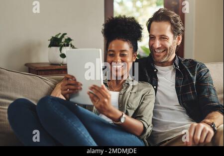 C'est ainsi que nous restons connectés avec le monde. un jeune couple heureux utilisant une tablette numérique ensemble tout en se relaxant sur un canapé à la maison. Banque D'Images
