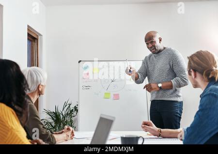 HES a tout planifié pour le T. un homme d'affaires mature discutant d'idées sur un tableau blanc avec ses collègues au travail. Banque D'Images