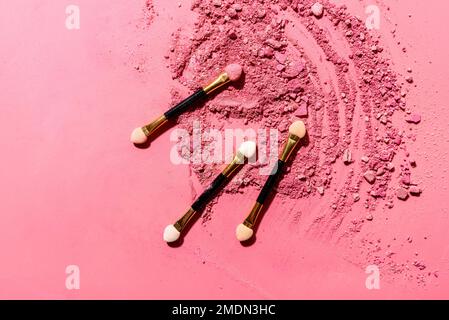 Ombres à paupières roses écrasées avec pinceau ou outil de mélange d'applicateur sur fond rose Banque D'Images