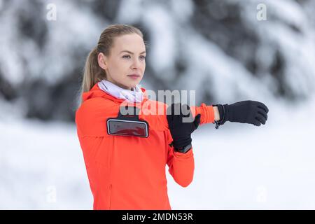 Coureur sportif faisant de l'exercice d'étirement, se préparant à l'entraînement dans le parc d'hiver enneigé. Banque D'Images