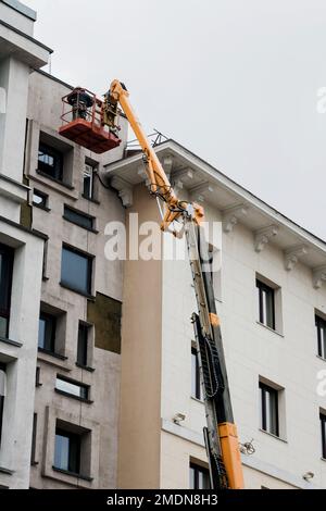 Ouvrier de construction dans le seau de levage de la grue restaurer et réparer la façade historique du bâtiment. Homme dans le berceau, restauration de la décoration en plâtre sur la façade Banque D'Images