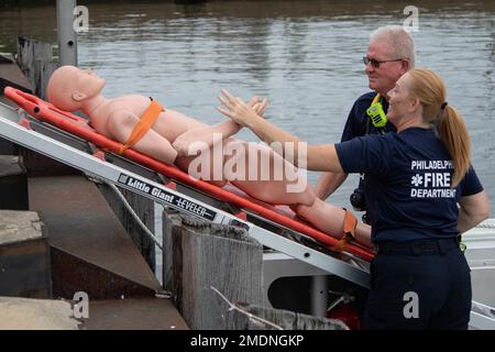 Le capitaine Stefani Gorman, officier des opérations maritimes, et Thomas Fry, ingénieur des pompiers, tous deux au service des incendies de Philadelphie, livrent une victime notionnelle au personnel de décontamination des victimes de masse affecté à la 140th Chemical Company, California National Guard, au Navy Yard, Philadelphie, Pennsylvanie. 26 juillet 2022. Le Groupe de travail 46 et plus de 600 membres du personnel de ses partenaires fédéraux, d'État, locaux, privés et universitaires ont collaboré à l'exercice le plus récent du terrain urbain dense (DUT). La série d’exercices de la TUT a débuté en 2018 et est devenue l’un des premiers à tous risques de la nation Banque D'Images
