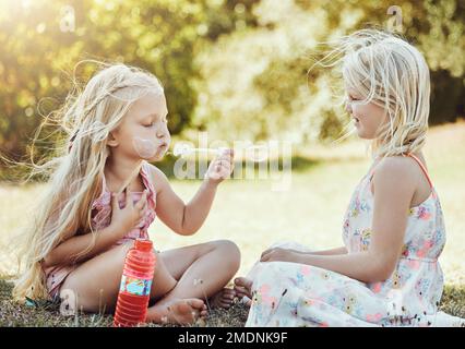 Nature, filles et amis soufflant des bulles dans un jardin vert étant ludique, heureux et amusant ensemble. Bonheur, vacances et sœurs jouant sur l'herbe Banque D'Images