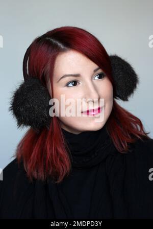 fille souriante à tête rouge dans les couvre-oreilles en fourrure et le foulard noir Banque D'Images