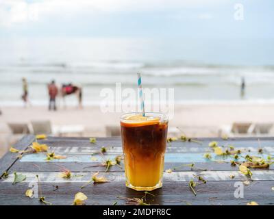 Un verre d'orange frais glacé americano décoré de tranches de ​​orange servi sur une table en bois sur le fond de la plage, vue sur la mer. Café noir froid Banque D'Images