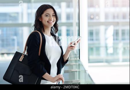 Le système IVE a chargé mon appareil avec les bonnes connexions. Portrait court d'une jeune femme d'affaires attrayante en souriant tout en utilisant un smartphone dans un moderne Banque D'Images