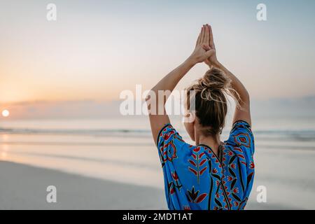 Vue arrière de la jeune femme faisant du yoga, la routine du matin et le concept de mode de vie sain. Banque D'Images