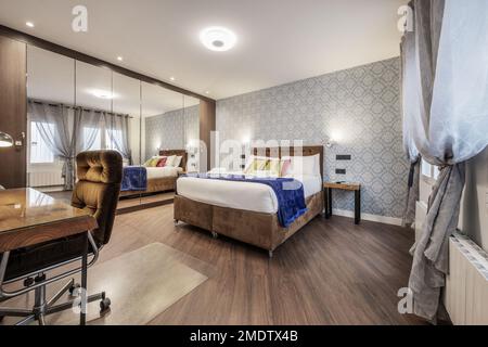 Chambre avec un mur couvert par une armoire intégrée avec portes en miroir, un lit double avec un canapé rembourré assorti avec roues, une tête de lit et un d Banque D'Images