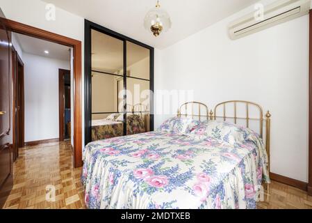 Chambre avec armoire intégrée à deux sections avec portes-miroirs coulissantes en aluminium noir et lit avec tête de lit en métal doré et une tête de lit en forme de méplat Banque D'Images