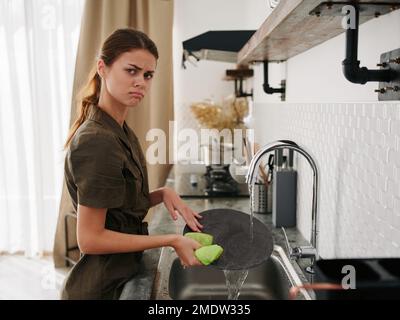 Femme fatiguée et irritée mains sans gants lave la vaisselle avec une éponge de lavage de vaisselle avec des bulles, des tâches ménagères, un look insatisfait, pas de lave-vaisselle Banque D'Images