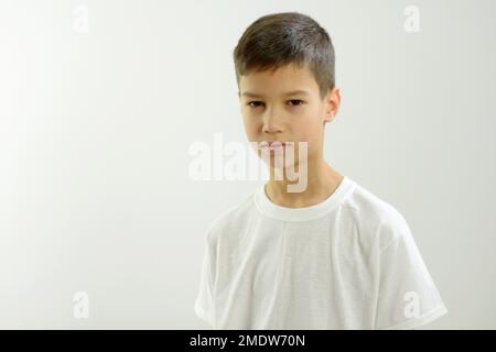 garçon de 8-10 ans regarde dans le cadre il y a place pour le texte fond blanc il est peu triste il a étroit les yeux orientaux belles lèvres soigné coiffure cheveux foncé t-shirt blanc peu reproachentilly Banque D'Images