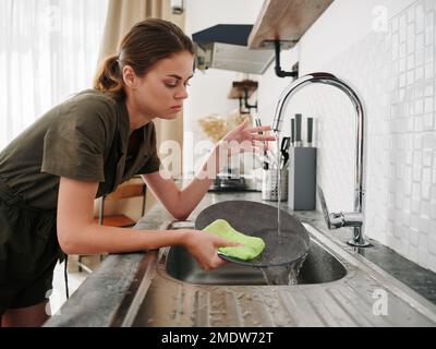 Femme fatiguée et fâchée mains sans gants lave la vaisselle avec une éponge de lave-vaisselle avec des bulles, des tâches ménagères, pas de lave-vaisselle, de l'eau élevée Banque D'Images