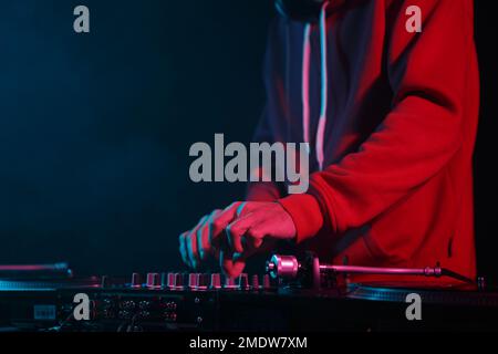 Club dj joue de la musique sur scène. Disc jockey en rouge à capuchon jouant des pistes musicales avec un mélangeur sonore et des platines en vinyle Banque D'Images