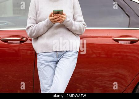 femme devant la porte latérale rouge voiture dans chaud pull-over bleu jeans Banque D'Images