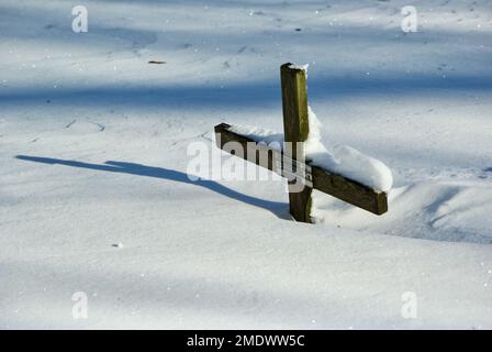 La croix en bois de l'ancien chrétien avec son ombre dans une forte dérive de neige sur le cimetière en hiver. Banque D'Images