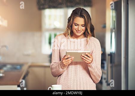 Les médias sociaux peuvent donner beaucoup de raisons de sourire. une jeune femme détendue prenant un café et utilisant un smartphone à la maison. Banque D'Images