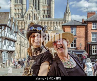 Deux femmes de steampunks amusants regardent directement l'appareil photo rire. La cathédrale de Lincoln est visible en arrière-plan. Banque D'Images