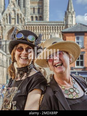 Deux femmes de steampunks amusants regardent directement l'appareil photo rire. La cathédrale de Lincoln est visible en arrière-plan. Banque D'Images