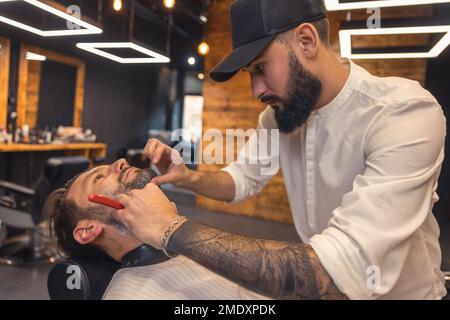 Coiffeur avec le bras à embout de tatouage, rasant soigneusement le client Banque D'Images