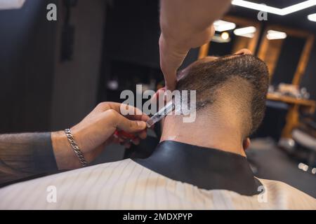 Coiffeur avec le bras à embout de tatouage, rasant soigneusement le client Banque D'Images