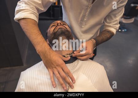 Coiffeur avec le bras à embout de tatouage, rasant soigneusement le client Banque D'Images