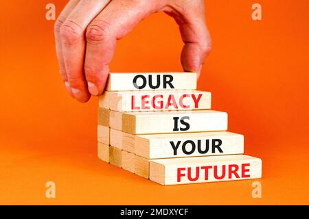 Symbole de l'héritage et du futur. Concept Words notre héritage est votre avenir sur des blocs de bois. Belle table orange fond orange. Main d'homme d'affaires. Buline Banque D'Images