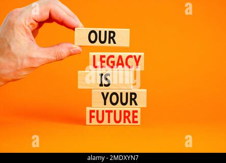 Symbole de l'héritage et du futur. Concept Words notre héritage est votre avenir sur des blocs de bois. Belle table orange fond orange. Main d'homme d'affaires. Buline Banque D'Images