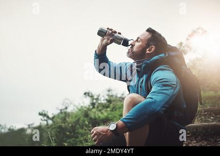 Juste ce dont j'avais besoin après un long voyage. un homme d'âge moyen assis et buvant de l'eau dans une bouteille dans les montagnes. Banque D'Images