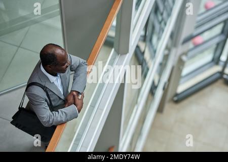 Photo ci-dessus d'un courtier afro-américain mature avec sac à main noir sur l'épaule debout près d'une rampe à l'intérieur d'un centre de bureau moderne Banque D'Images
