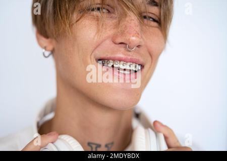 Portrait élégante blonde cheveux courts avec perçage du visage et bretelles dentaires regardant l'appareil photo et souriant sur fond blanc. Banque D'Images