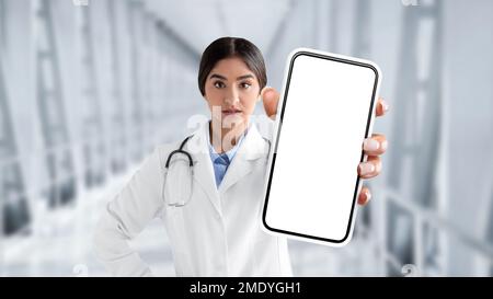 Femme indienne sérieuse médecin en uniforme montrant un écran de smartphone vide à l'appareil photo Banque D'Images