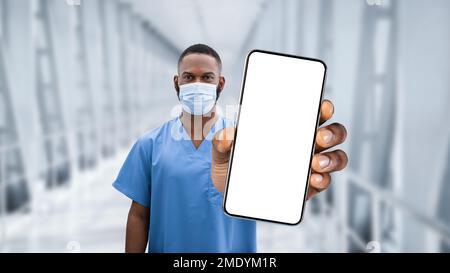 Modèle médical. Noir médecin dans le masque de protection montrant le smartphone avec écran vide Banque D'Images