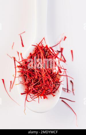 Safran en cuillère blanche sur fond blanc. Filets naturels secs de safran de fleurs de crocus. Banque D'Images