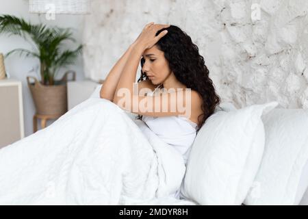 Une malheureuse femme maurie du millénaire arabe s'est réveillée, assise sur un lit blanc, couvrant le visage avec les mains Banque D'Images