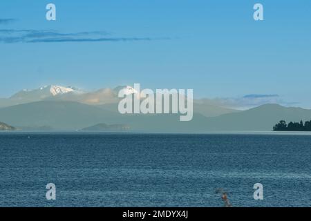 Vue sur le lac Taupo avec les montagnes enneigées du parc national de Tongariro à distance. Banque D'Images