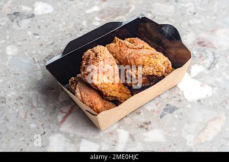 Gros plan des ailes de poulet frites dans de la pâte. Dans un restaurant de restauration rapide, il y a une boîte en carton de poulet sur la table. Banque D'Images