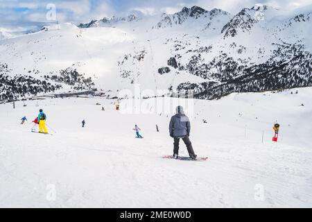 Snowboarders et skieurs qui descendent la montagne vers la vallée en contrebas avec des sommets enneigés en arrière-plan, Andorre, Pyrénées Banque D'Images