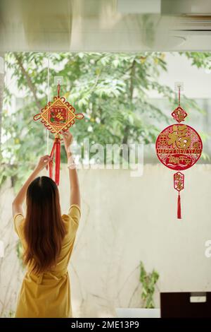 Mains de femme accrochant un pédant rond sur le mur pour décorer la maison pour le festival lunaire avec une bonne inscription de nouvel an Banque D'Images