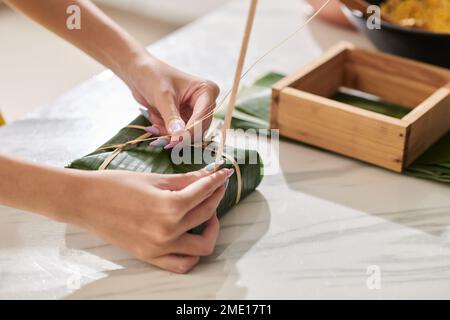 Mains de la femme emballant des gâteaux de riz collants dans des feuilles de banane Banque D'Images