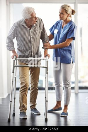 C'est tout. Une étape à la fois. Prise de vue en longueur d'une infirmière féminine mature qui aide son patient mâle âgé à utiliser son marcheur. Banque D'Images