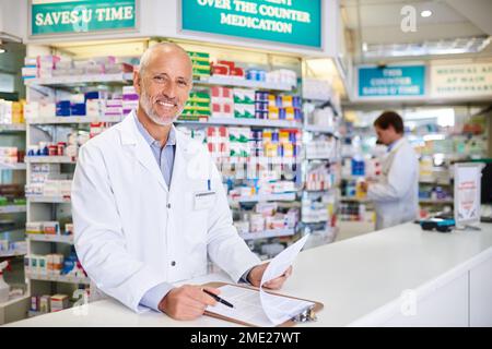 Ma passion réside dans l'industrie pharmaceutique. Portrait d'un pharmacien mature écrivant sur un bloc-notes dans un chimiste. Banque D'Images