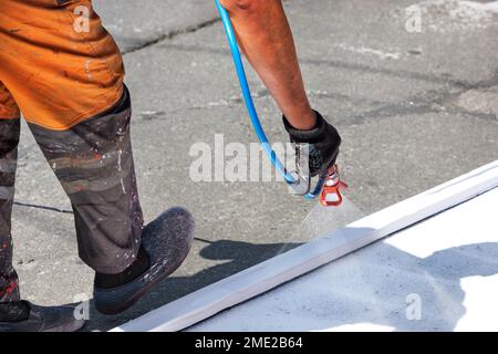 Un ouvrier de la route peint les marquages routiers d'un passage piéton lors d'un après-midi d'été chaud. Banque D'Images