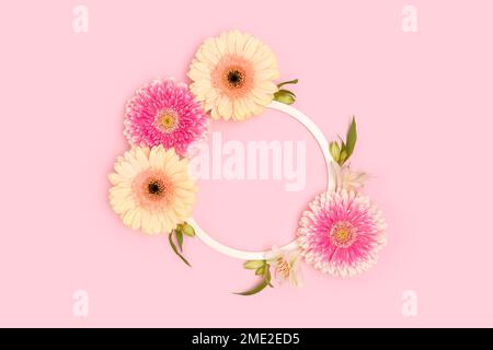 Couronne faite de feuilles vertes, d'alstroemeria et de fleurs de gerbera sur fond rose. Banque D'Images